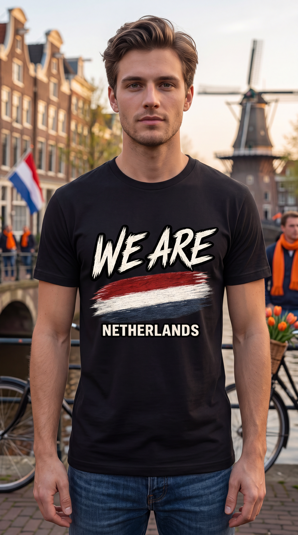 A man wearing a black t-shirt with a graphic that reads 'WE ARE NETHERLANDS' and a red, white, and blue paint stroke design, standing in front of a canal and windmill background.