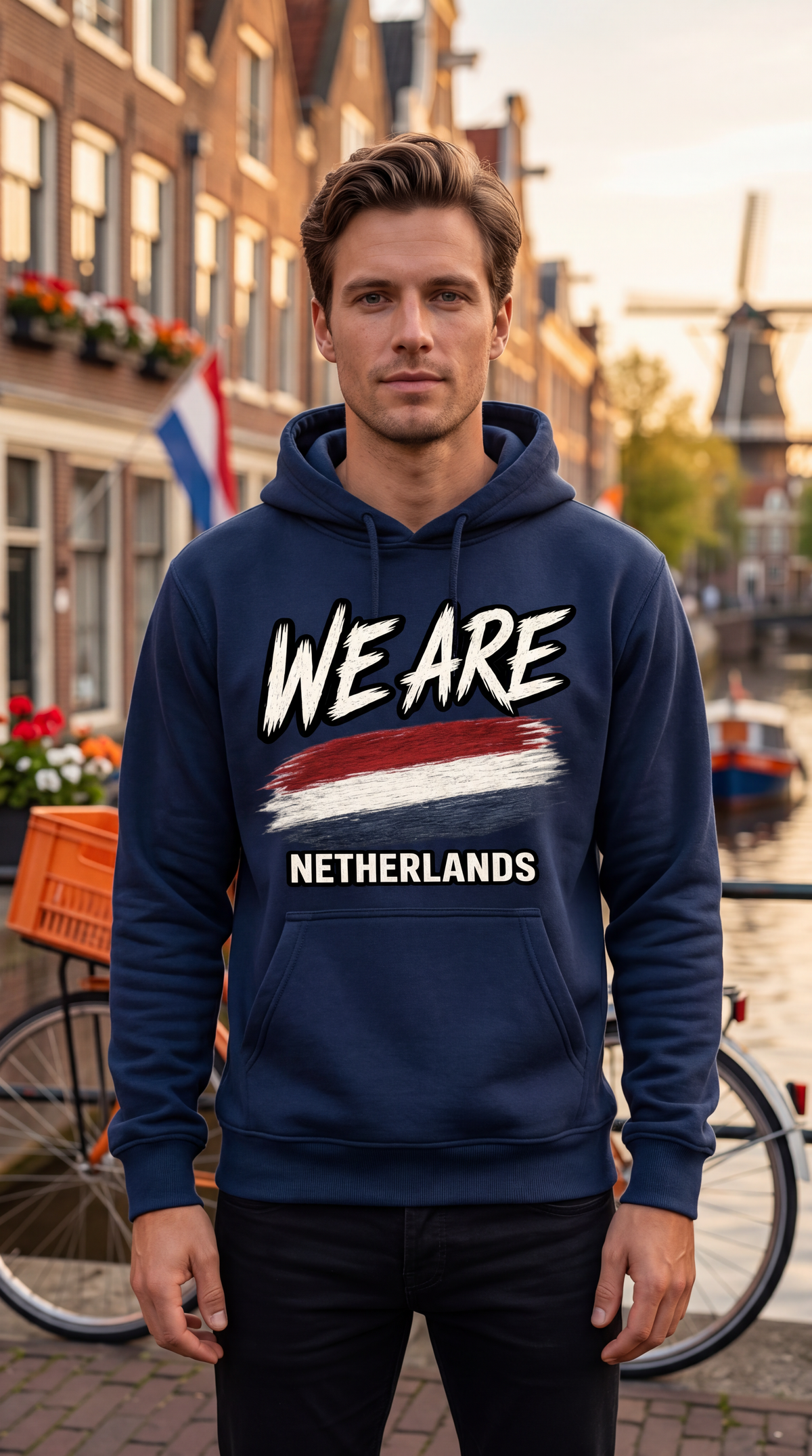 A man wearing a navy blue hoodie with 'WE ARE NETHERLANDS' and a red, white, and blue flag graphic printed on the chest, standing in front of a blurred canal-side street background.