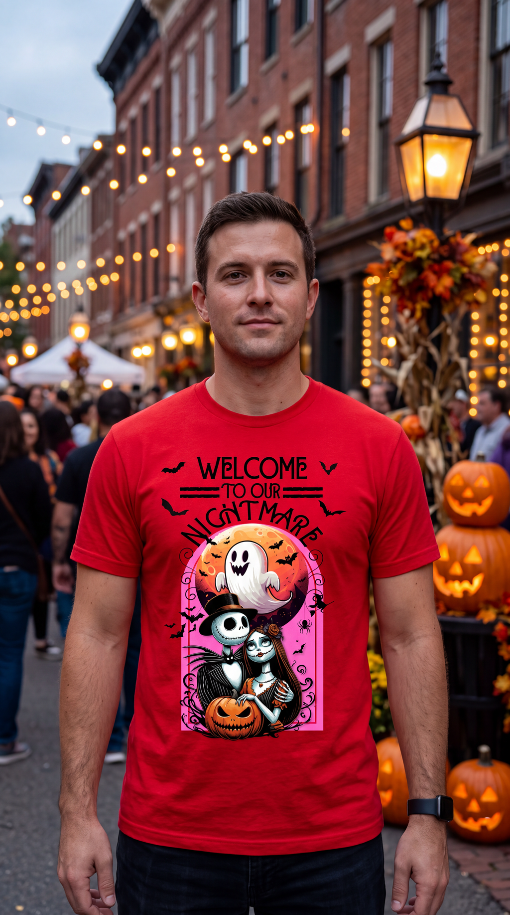 A man wearing a bright red graphic t-shirt with a Halloween-themed design that reads 'WELCOME TO OUR NIGHTMARE' and features Jack Skellington and a ghost holding a pumpkin, standing in a Halloween-decorated street with pumpkins and string lights.