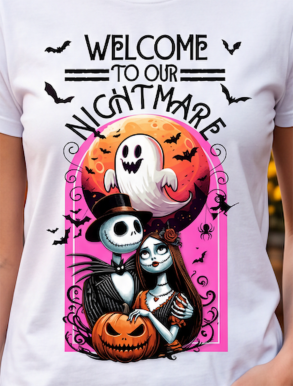 A white short-sleeve T-shirt worn by a person, featuring a large Halloween graphic print with the text 'WELCOME TO OUR NIGHTMARE' above Jack Skellington and Sally in front of a moon and bats.