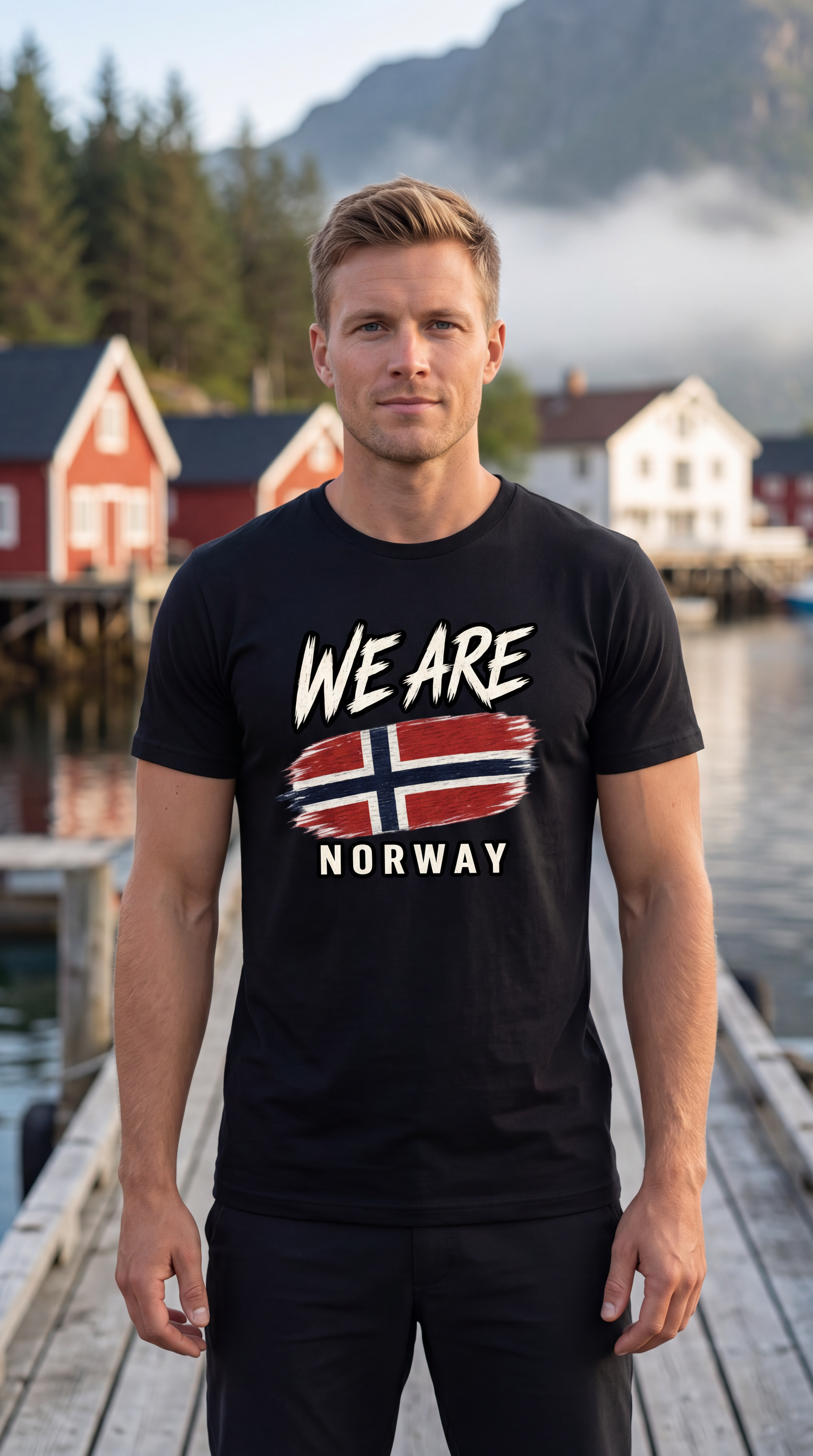 A man standing on a wooden dock wearing a black t-shirt with a graphic that reads 'WE ARE NORWAY' and features the Norwegian flag. The background shows a scenic view of a Norwegian coastal town with red houses, water, and mountains.