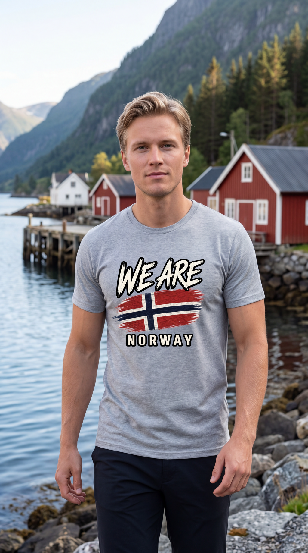 A man wearing a heather gray t-shirt with a 'WE ARE NORWAY' graphic featuring the Norwegian flag, standing in front of a scenic fjord backdrop with red cabins and mountains.