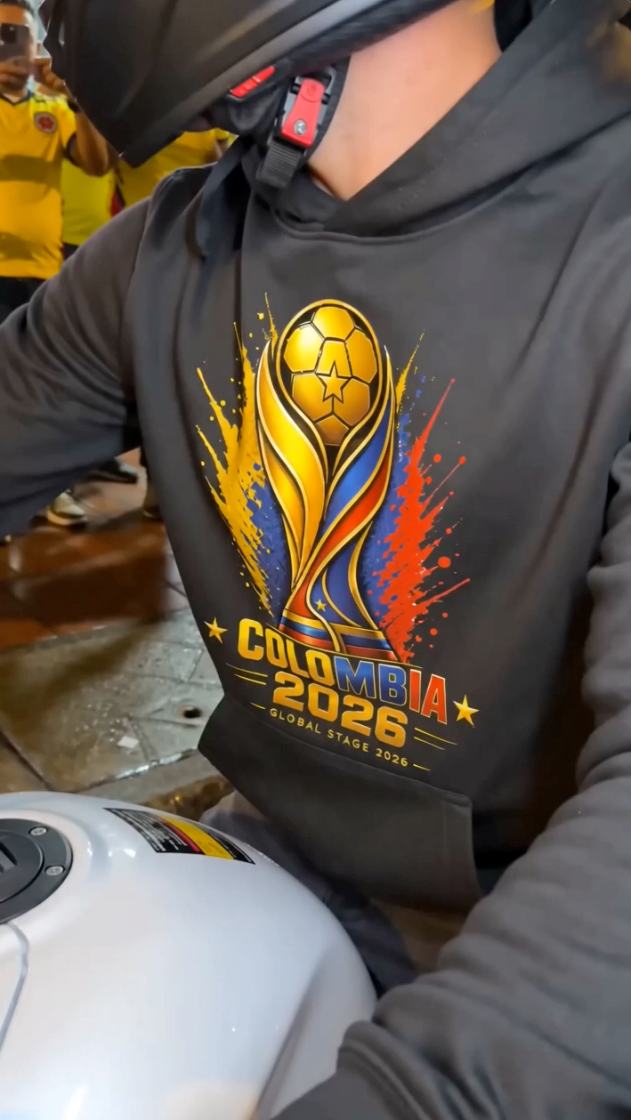 Person wearing black Colombia 2026 soccer hoodie with yellow blue and red football-inspired graphic while riding motorcycle