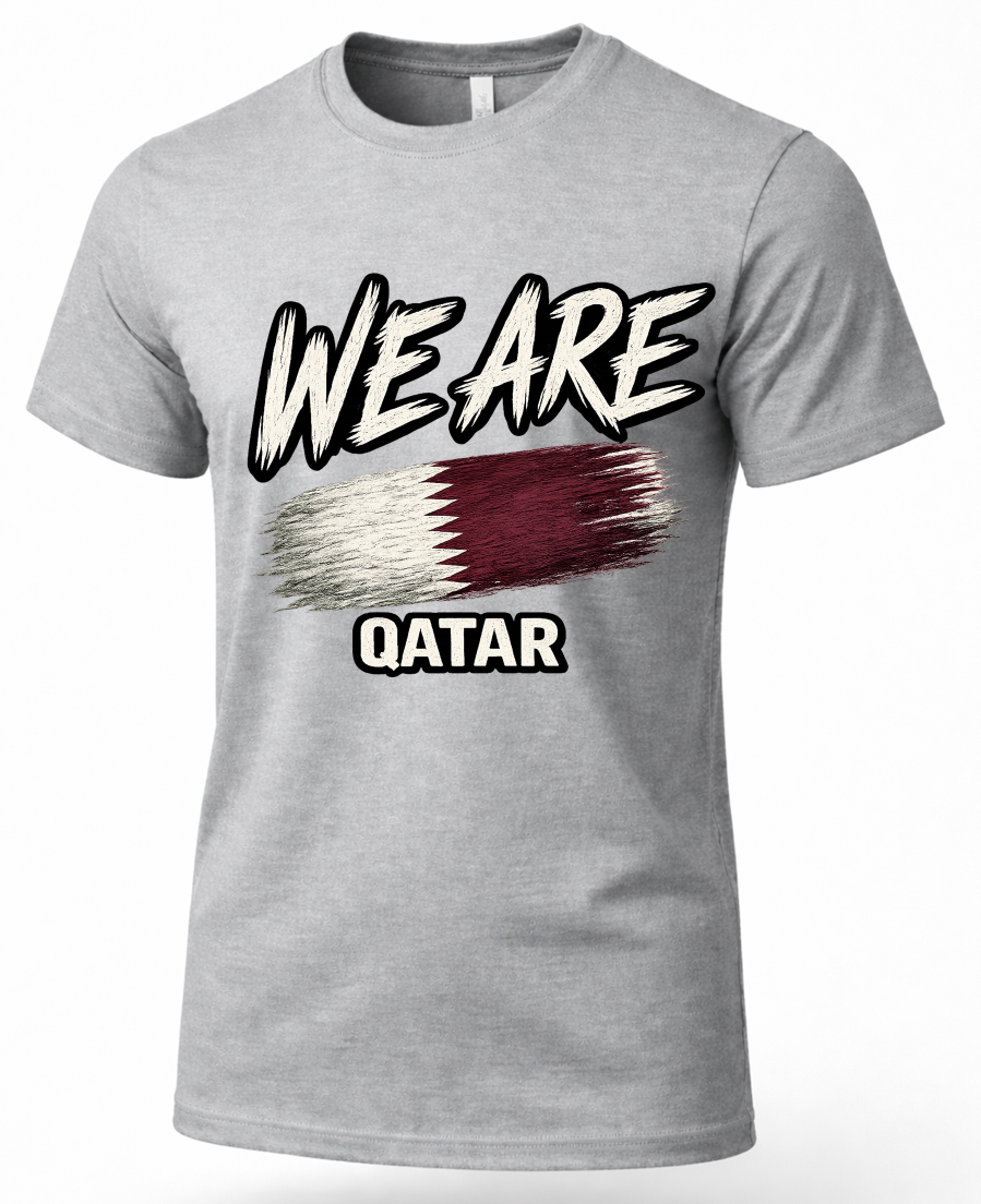 A heather gray short-sleeve t-shirt with a graphic print on the front. The graphic features the text 'WE ARE' in a stylized white and black brush-stroke font, a horizontal flag design in white and dark red, and the word 'QATAR' below in white block letters with a black outline.