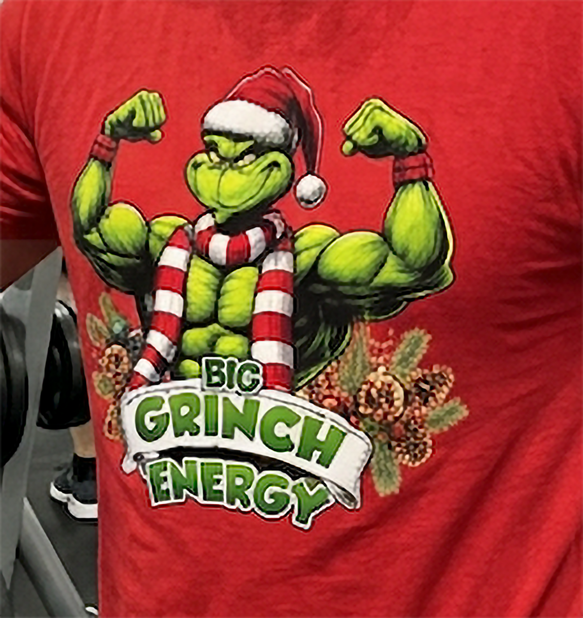 Close-up of Big Grinch Energy Christmas graphic on red t-shirt featuring muscular green Grinch and colorful holiday decorations.