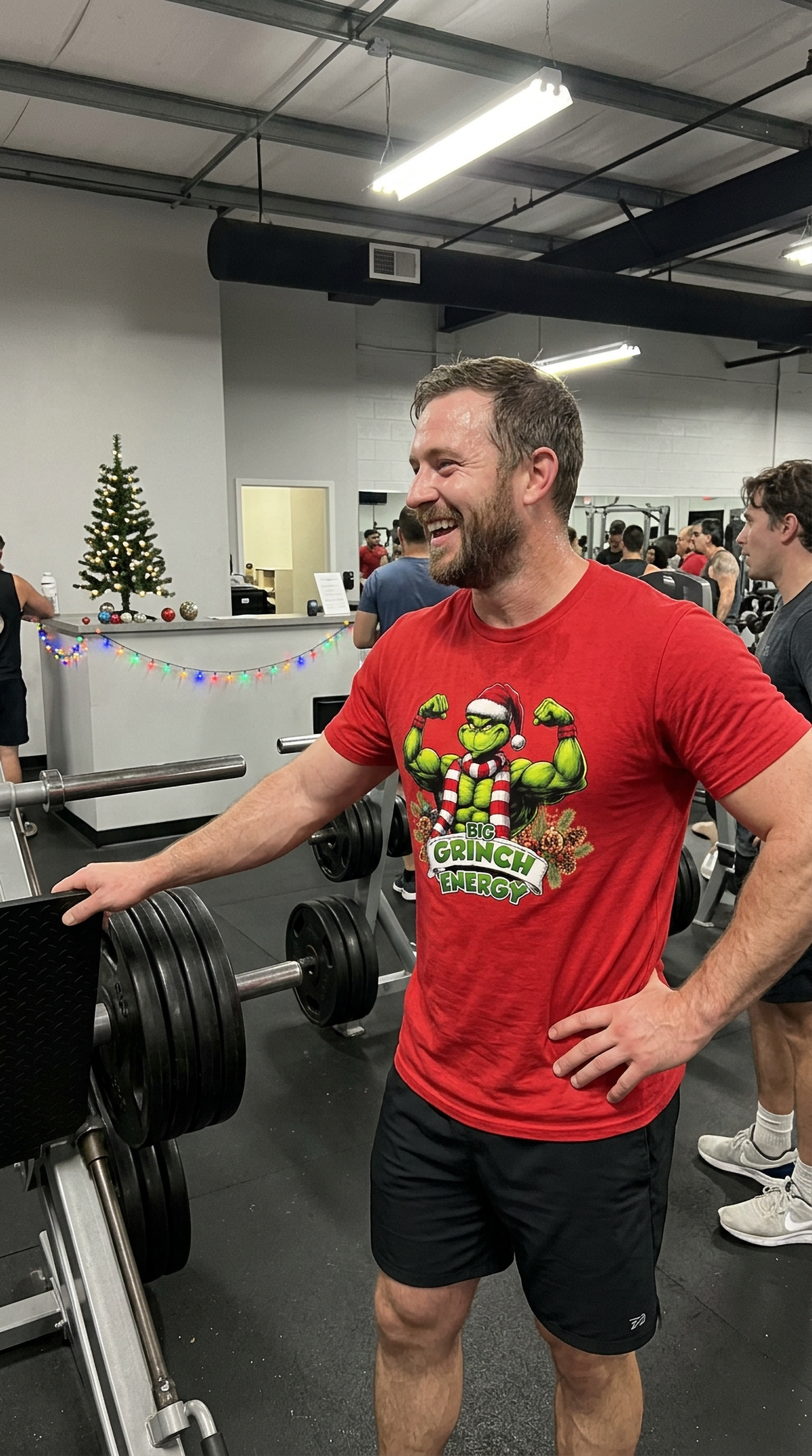Man wearing red Big Grinch Energy Christmas t-shirt at the gym featuring muscular green Grinch artwork and festive holiday design.
