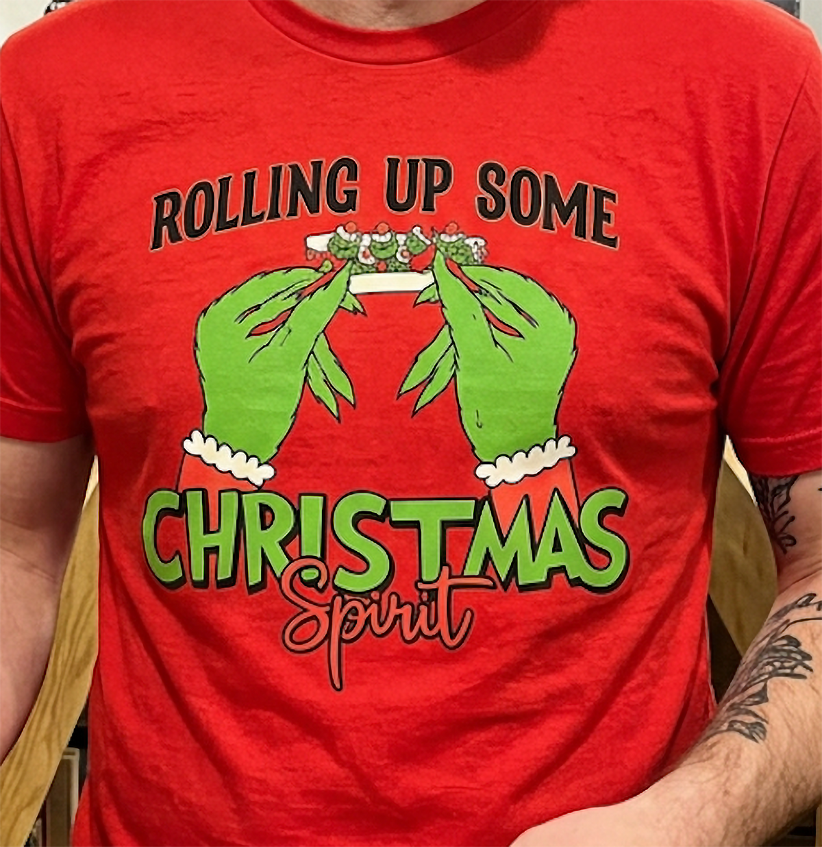 Close-up of red Rolling Up Some Christmas Spirit shirt highlighting green hands, Santa sleeves, and festive holiday typography.