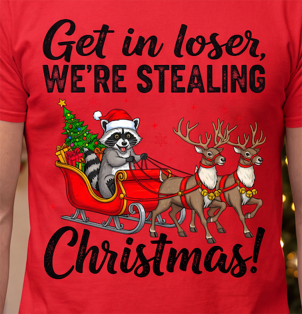 Close-up of Get in Loser We’re Stealing Christmas raccoon, sleigh and reindeer graphic on a red T-shirt.