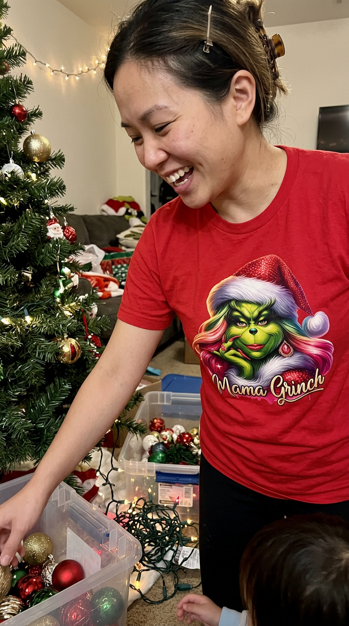 Woman wearing red Mama Grinch Christmas t-shirt while preparing gifts at a holiday gathering.