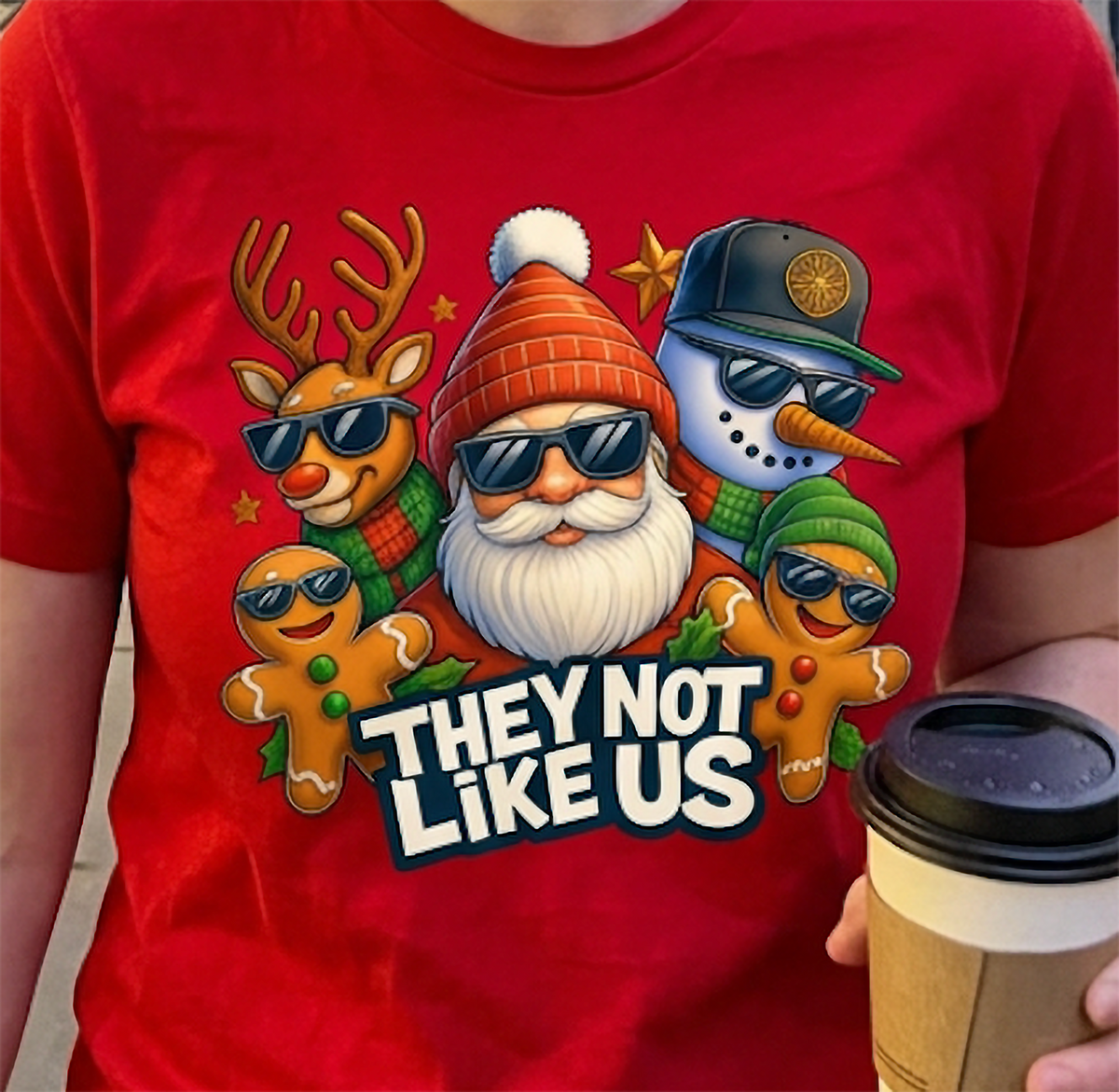Close-up of red They Not Like Us Christmas shirt featuring colorful holiday character artwork and bold white lettering.
