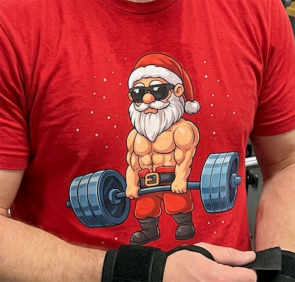 Close-up of Swole Santa Christmas gym artwork on a red t-shirt featuring Santa wearing sunglasses and holding a barbell.