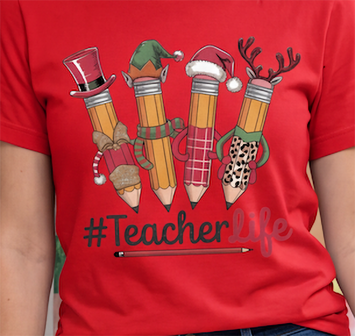 Close-up of red Teacher Life Christmas shirt showing Santa, elf, snowman and reindeer pencil design.