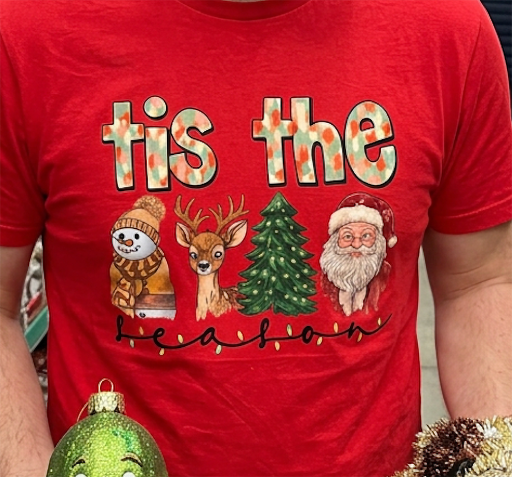 Close-up of red Tis the Season Christmas shirt highlighting festive watercolor holiday characters and decorative seasonal lettering.
