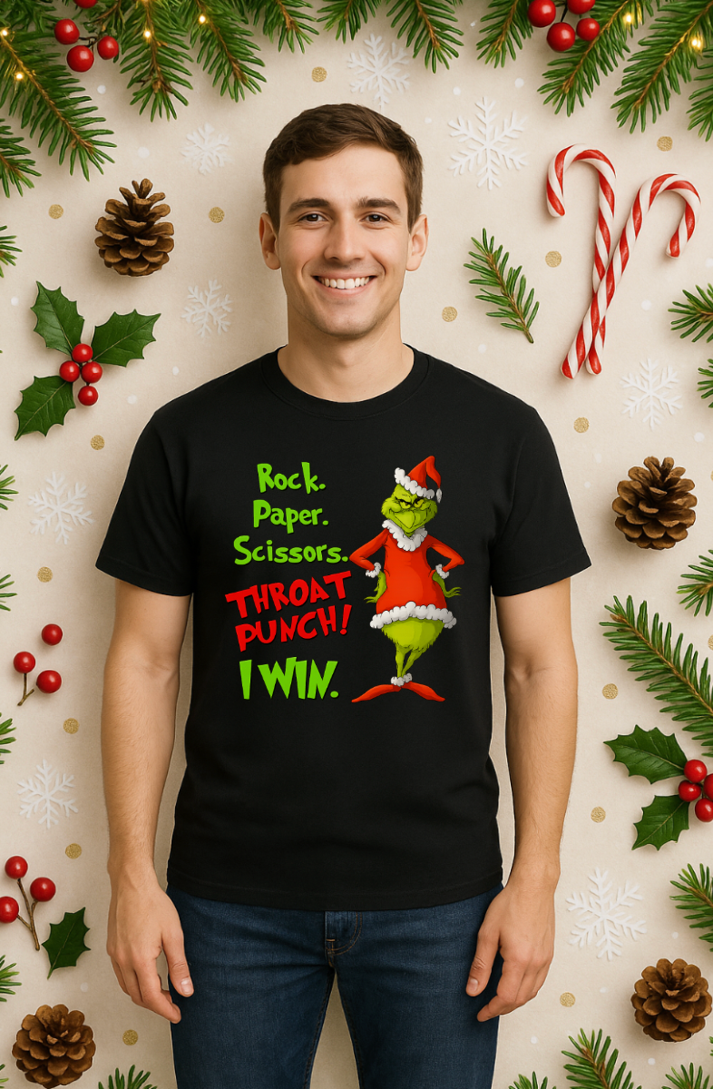 Man wearing a black Christmas graphic t-shirt featuring a green mischievous character in a red Santa outfit with the phrase “Rock. Paper. Scissors. Throat Punch! I Win.” standing in front of a festive background with candy canes, holly, pine branches, and ornaments.