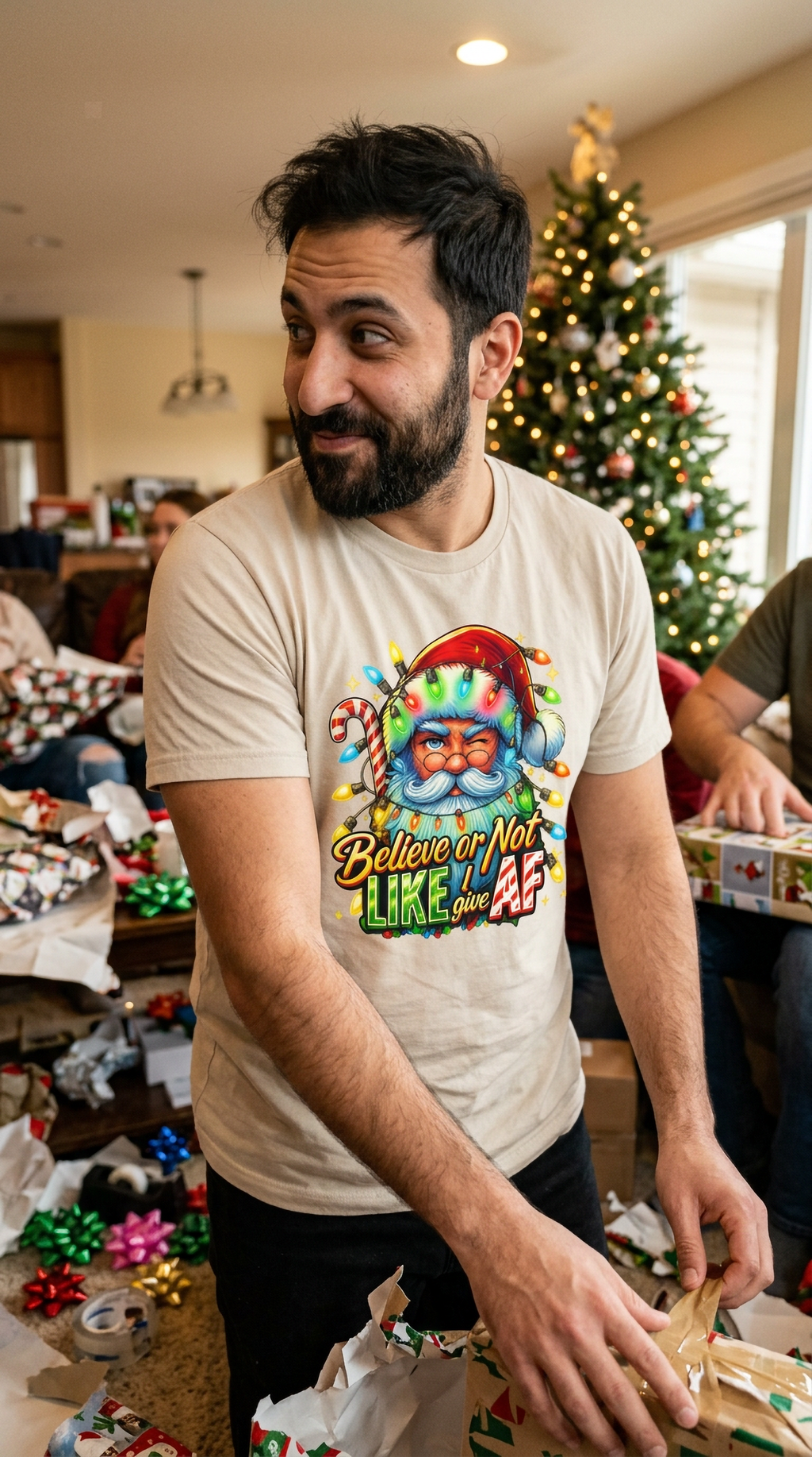 Lifestyle – Sand: Man wearing a sand-colored Believe or Not funny Christmas t-shirt at a casual indoor holiday celebration.