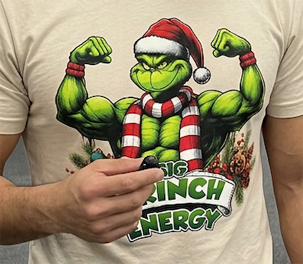 Close-up of Big Grinch Energy Christmas design on sand-colored t-shirt with muscular Grinch illustration and bold holiday lettering.