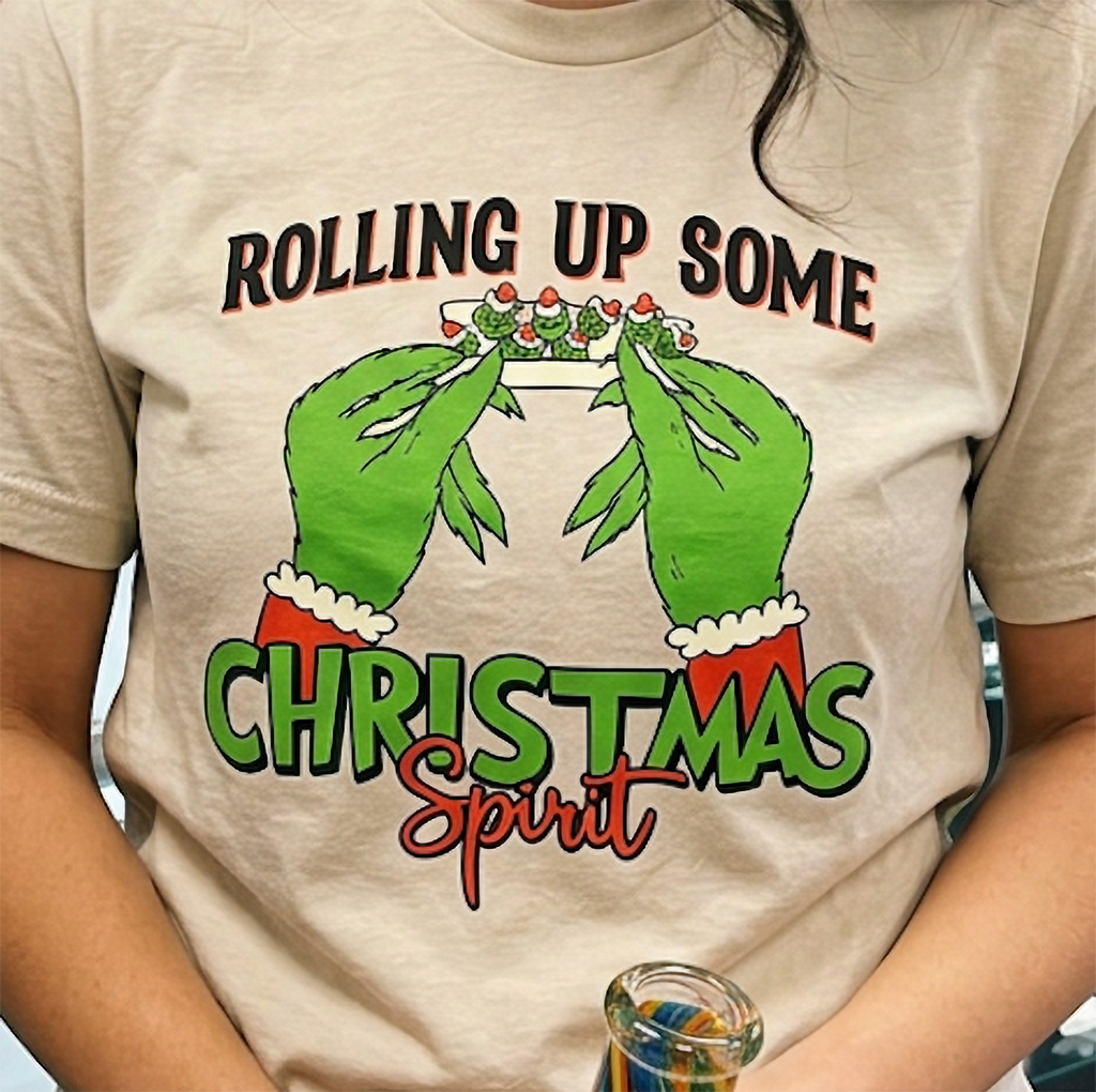 Close-up of sand Christmas t-shirt showing detailed cannabis-inspired holiday artwork and festive lettering.