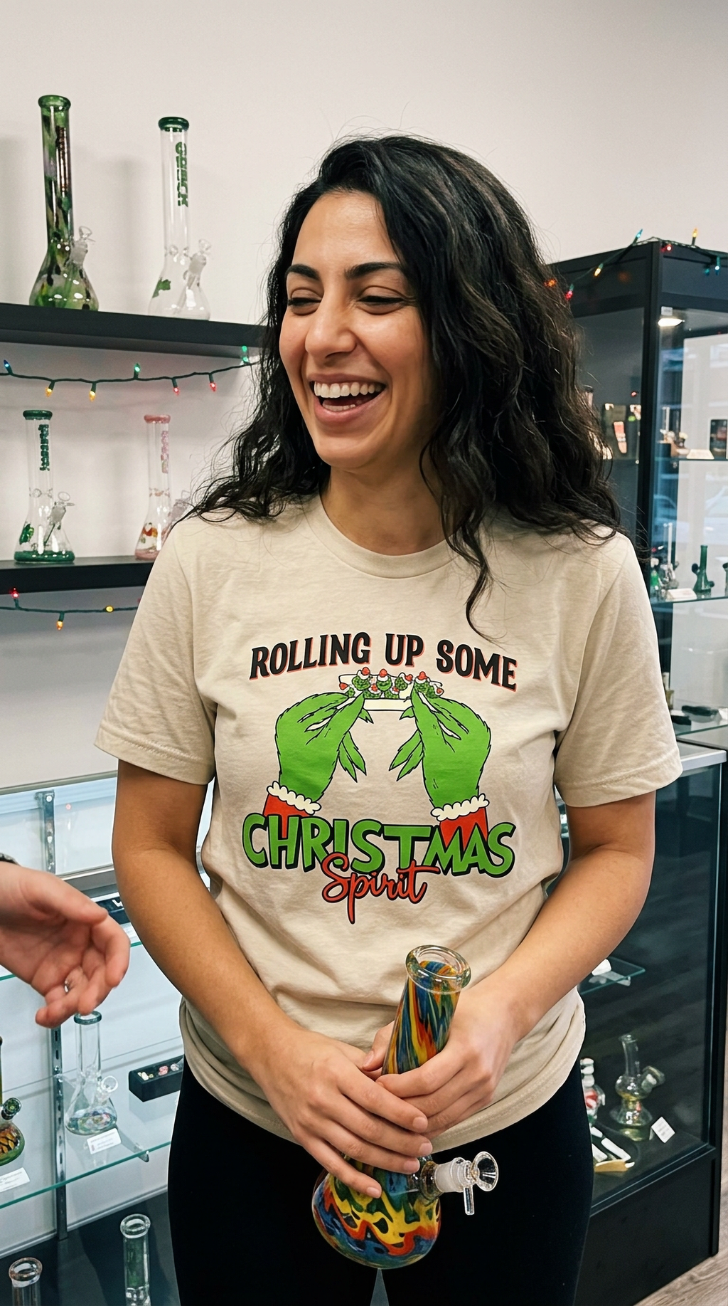 Woman wearing sand-colored Rolling Up Some Christmas Spirit t-shirt while standing inside a store.