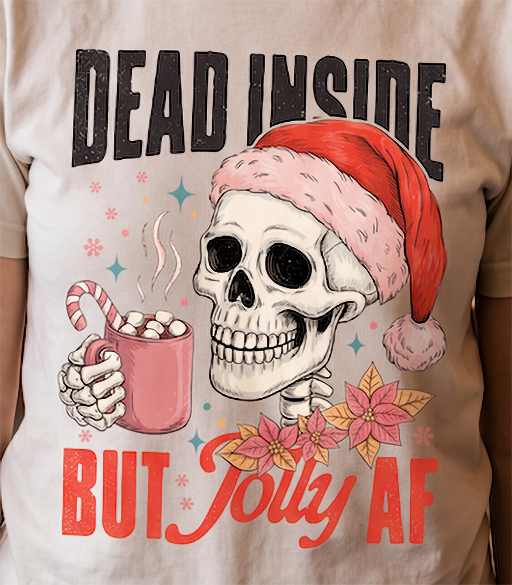 Close-up of Dead Inside But Jolly AF skeleton Santa Christmas graphic printed on sand shirt.