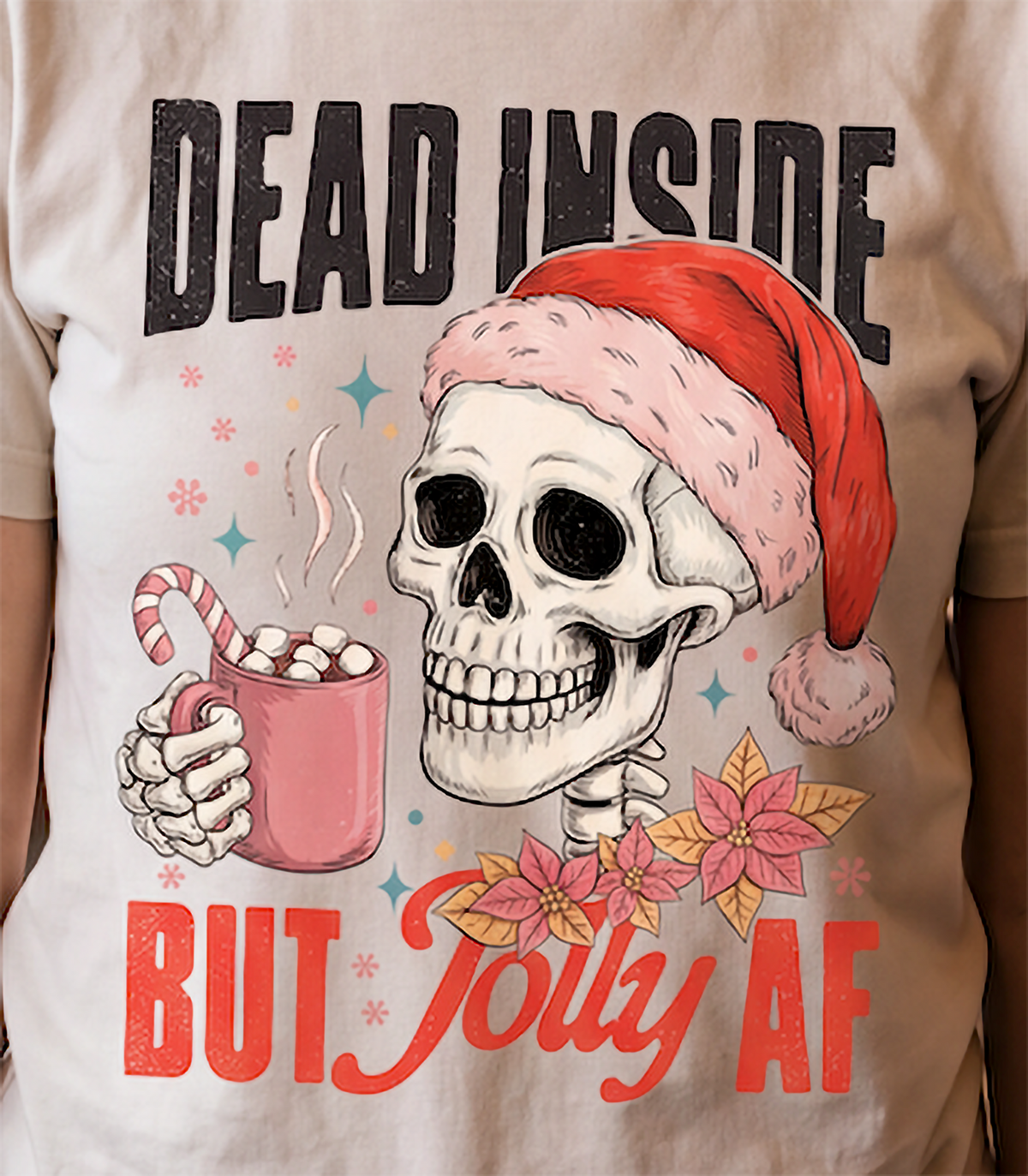 Close-up of Dead Inside But Jolly AF skeleton Santa Christmas graphic printed on sand shirt.