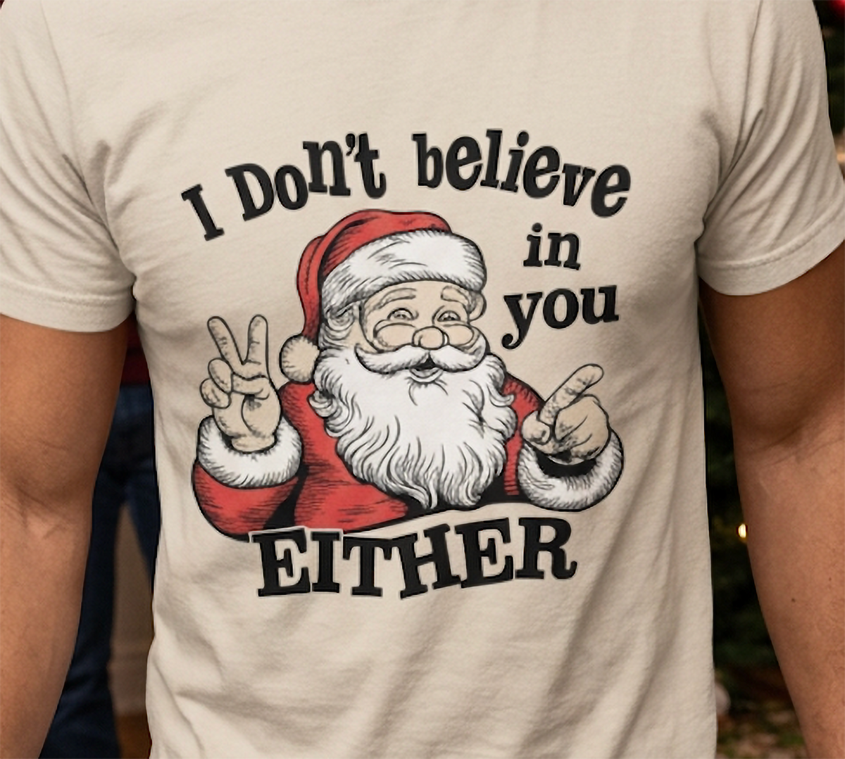 Close-up of sand Christmas graphic tee showing Santa Claus pointing with bold black and white holiday lettering.