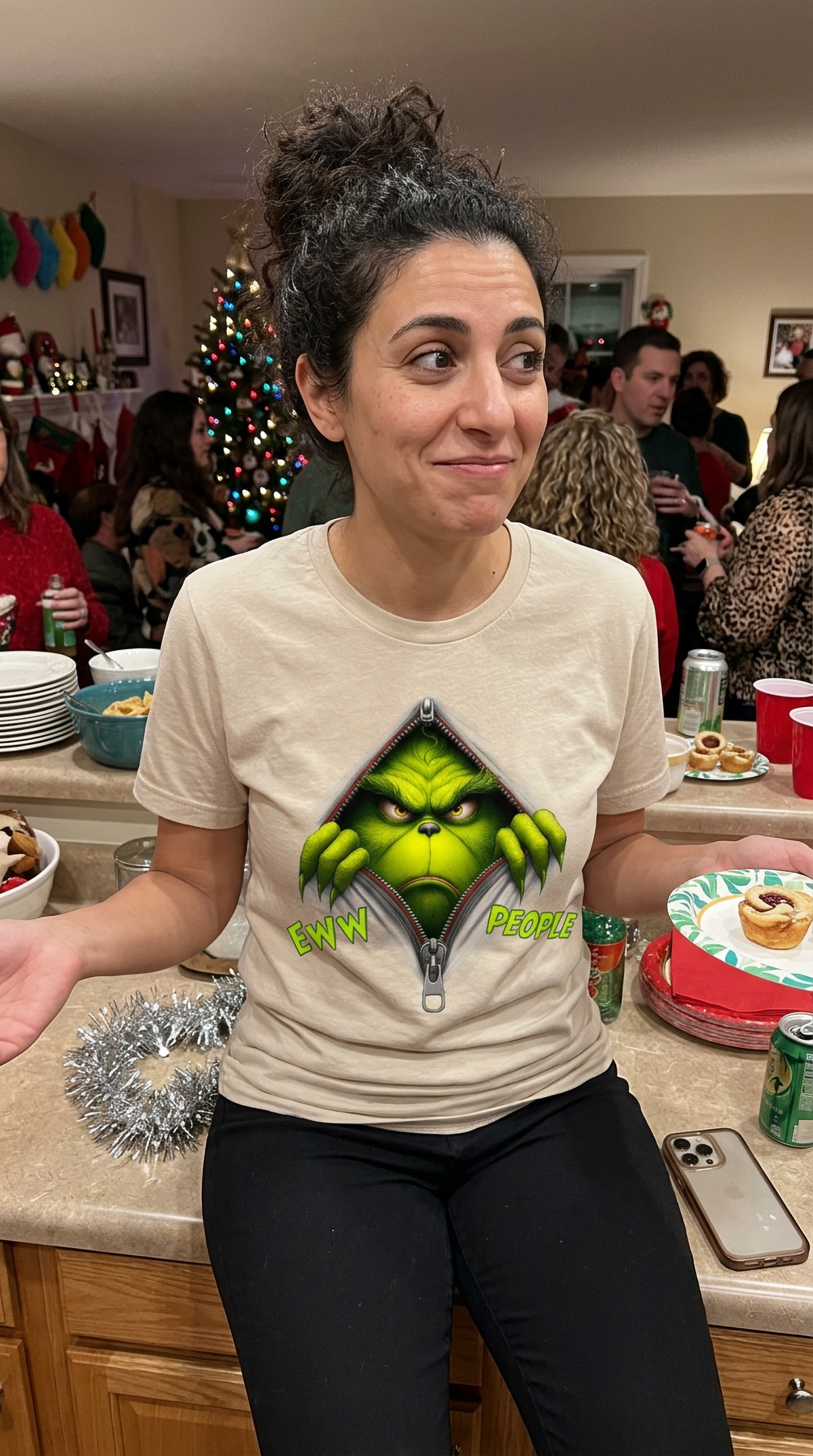 Sand Lifestyle: Person wearing a sand-colored Eww People Grinch graphic t-shirt during a festive holiday gathering.