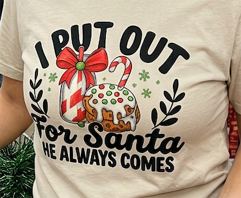 Close-up of I Put Out for Santa He Always Comes graphic on sand Christmas shirt