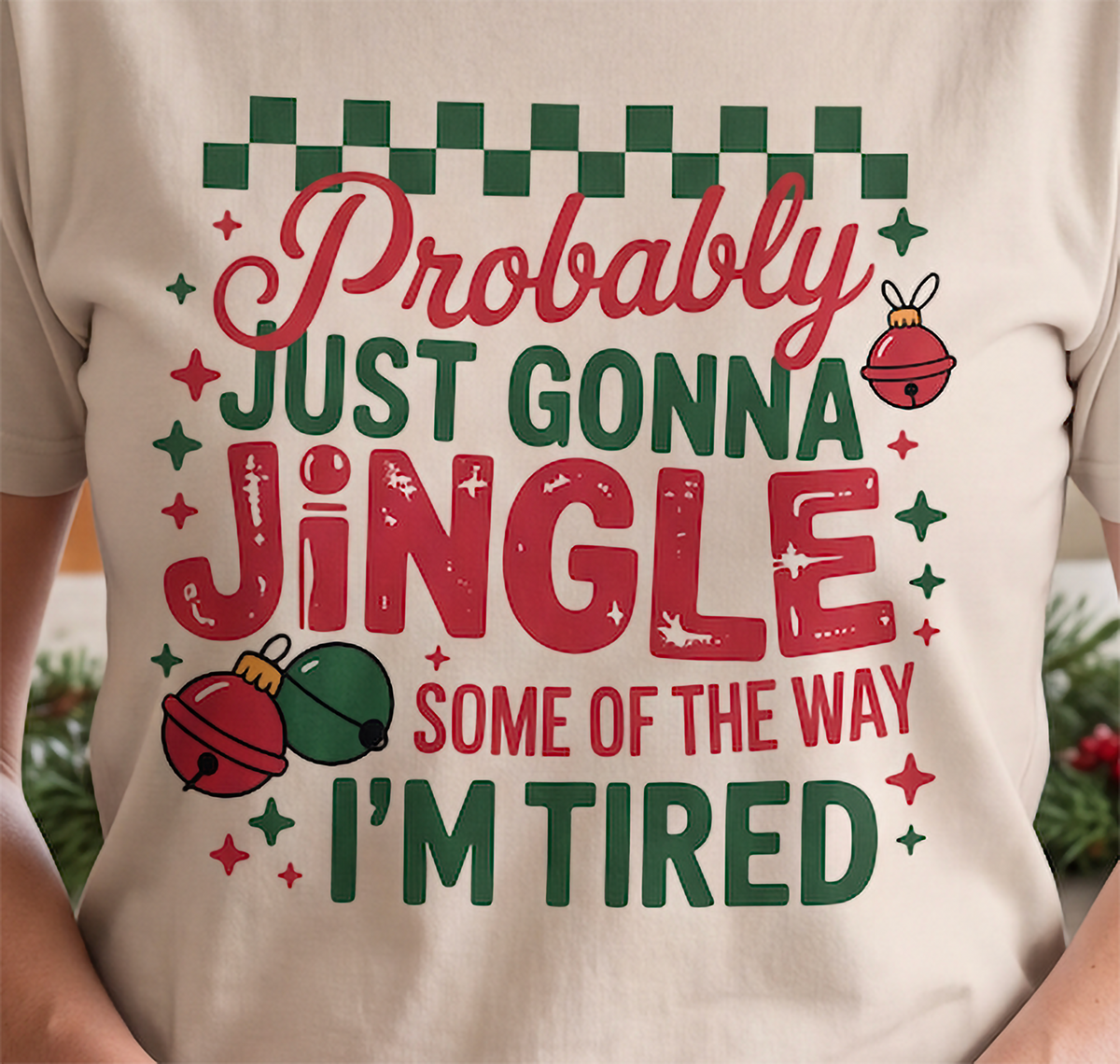 Close-up of Probably Just Gonna Jingle Some of the Way I’m Tired Christmas graphic on a sand T-shirt.