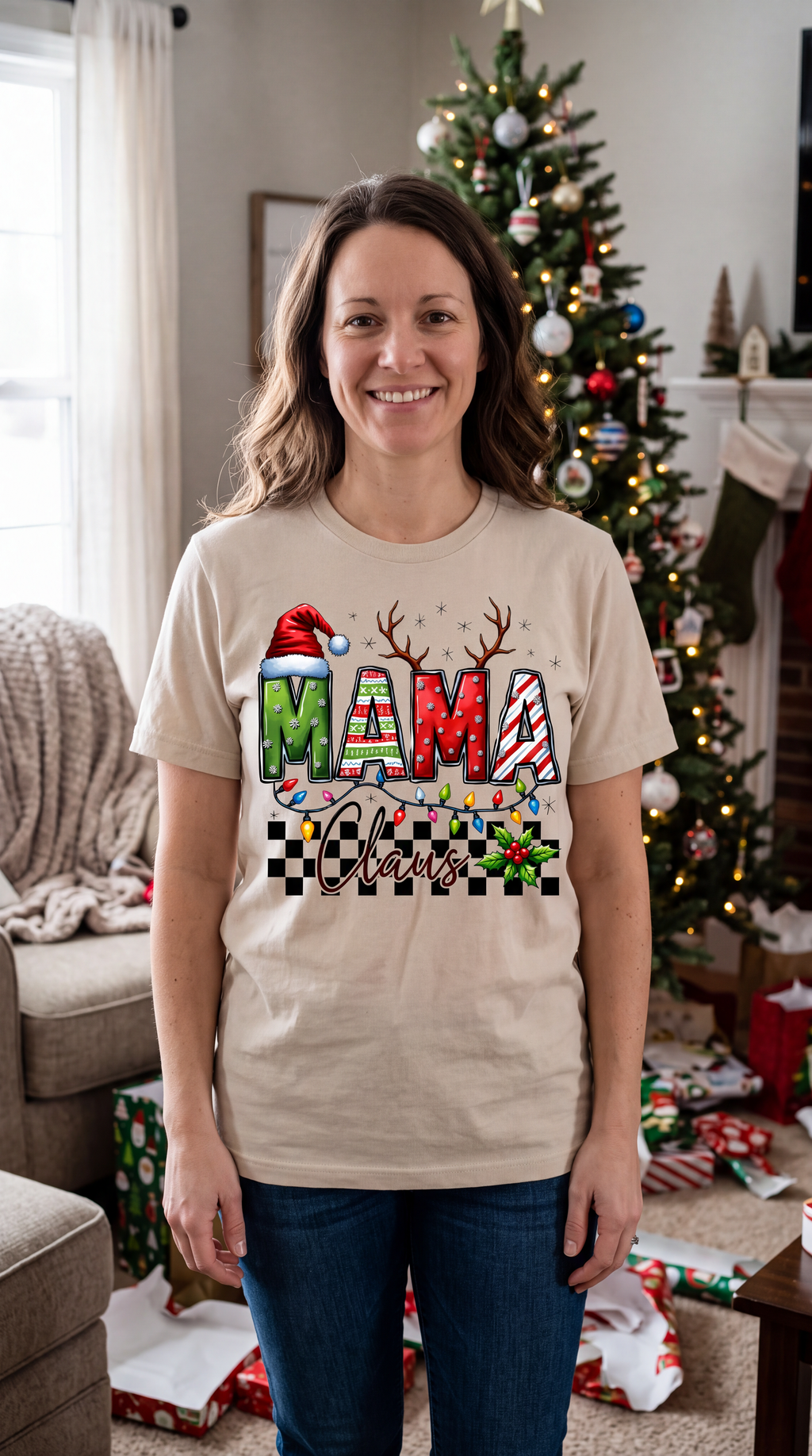 Woman wearing sand Mama Claus Christmas graphic shirt indoors beside a decorated Christmas tree.