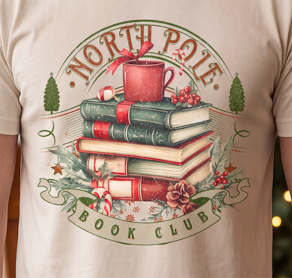 Close-up of North Pole Book Club Christmas design on sand graphic shirt with cozy holiday reading theme.