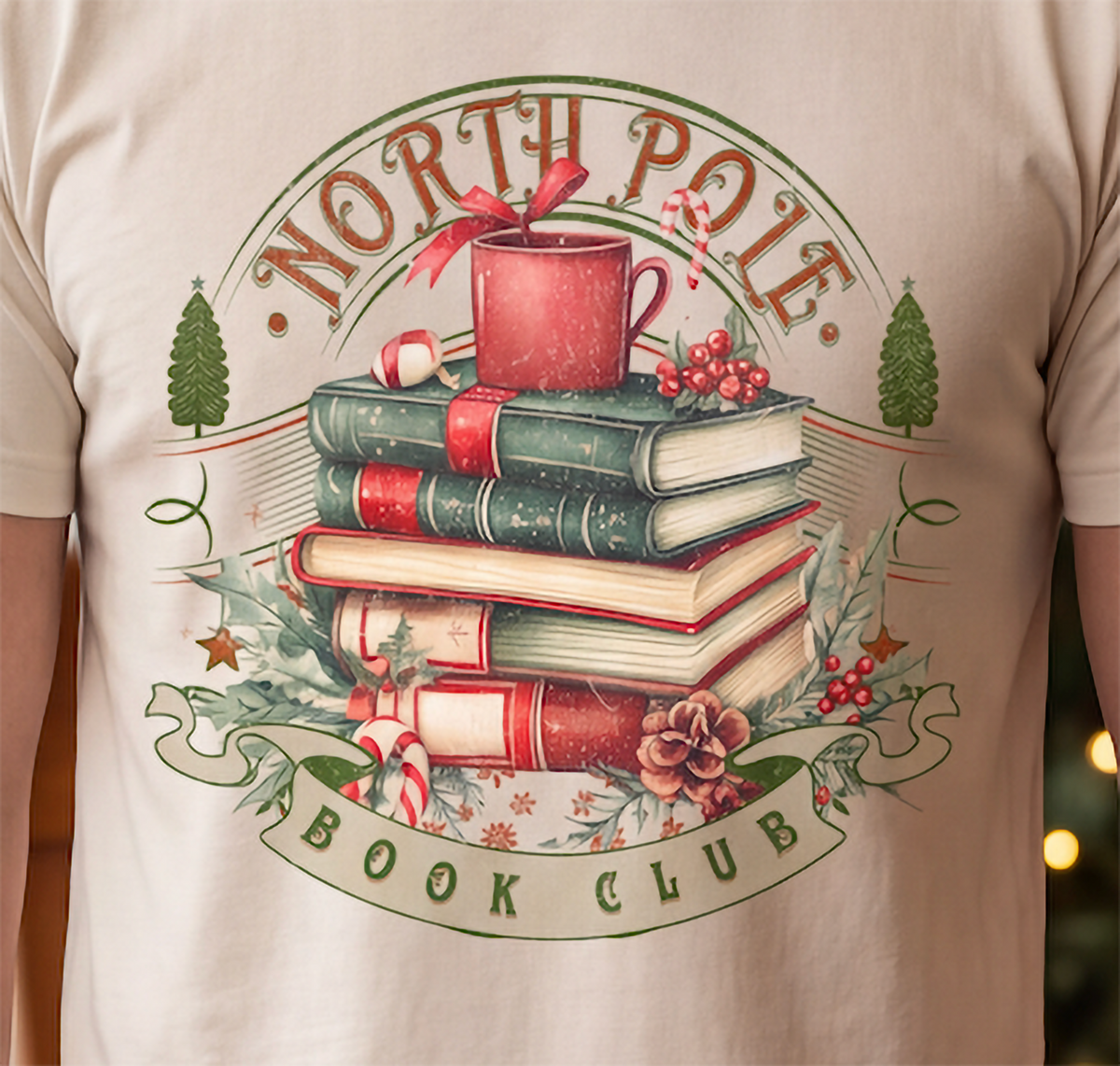 Close-up of North Pole Book Club Christmas design on sand graphic shirt with cozy holiday reading theme.
