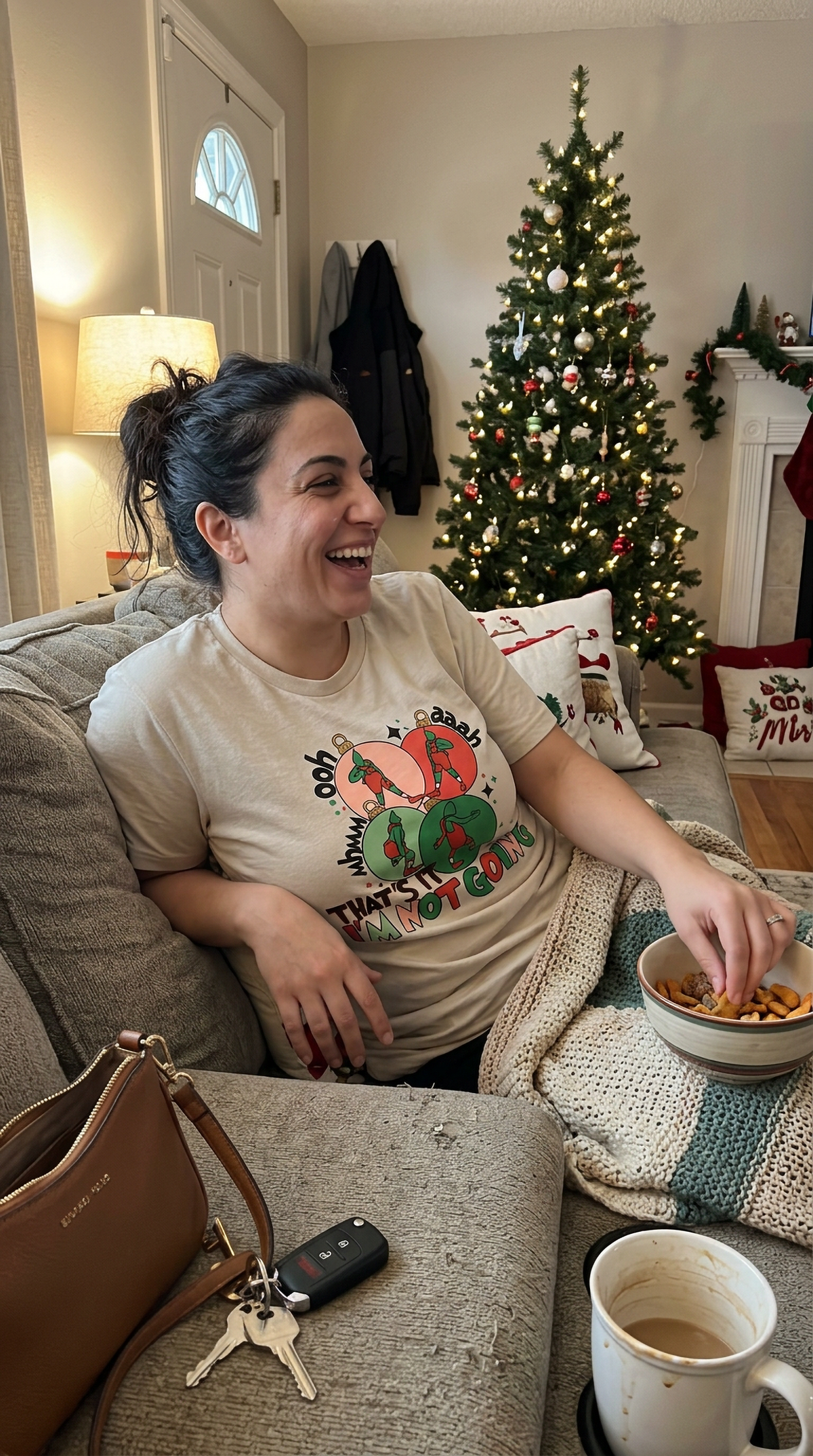 Sand Lifestyle: Woman wearing a sand-colored funny Christmas graphic t-shirt while relaxing at a festive indoor gathering.