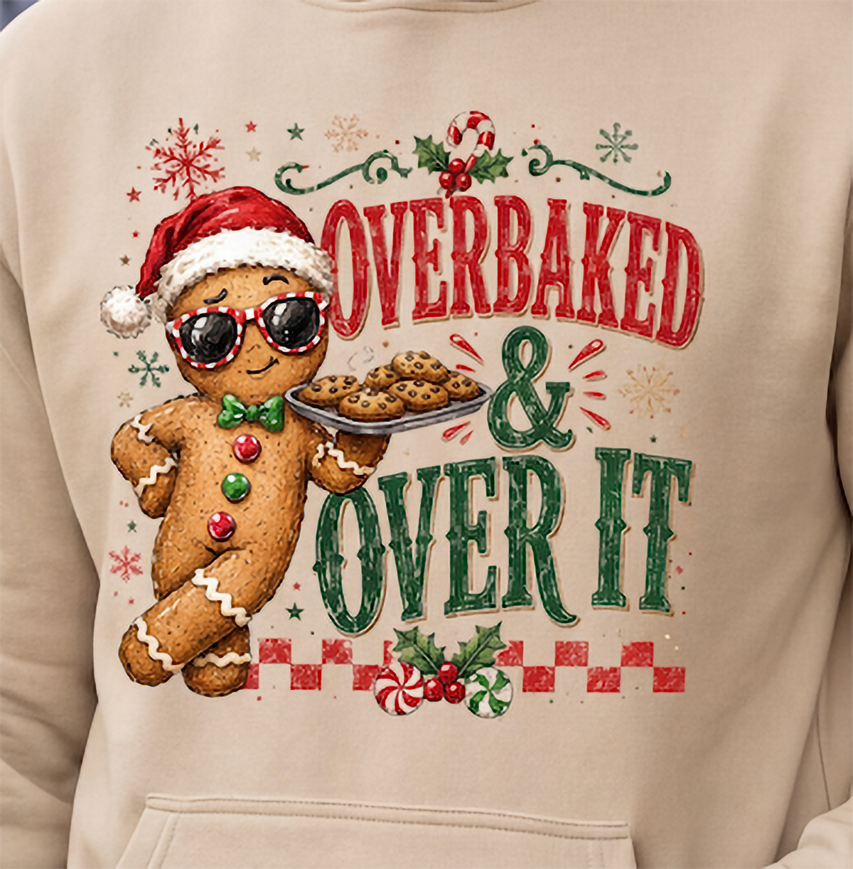 Close-up of sand Overbaked and Over It Christmas hoodie with gingerbread man design