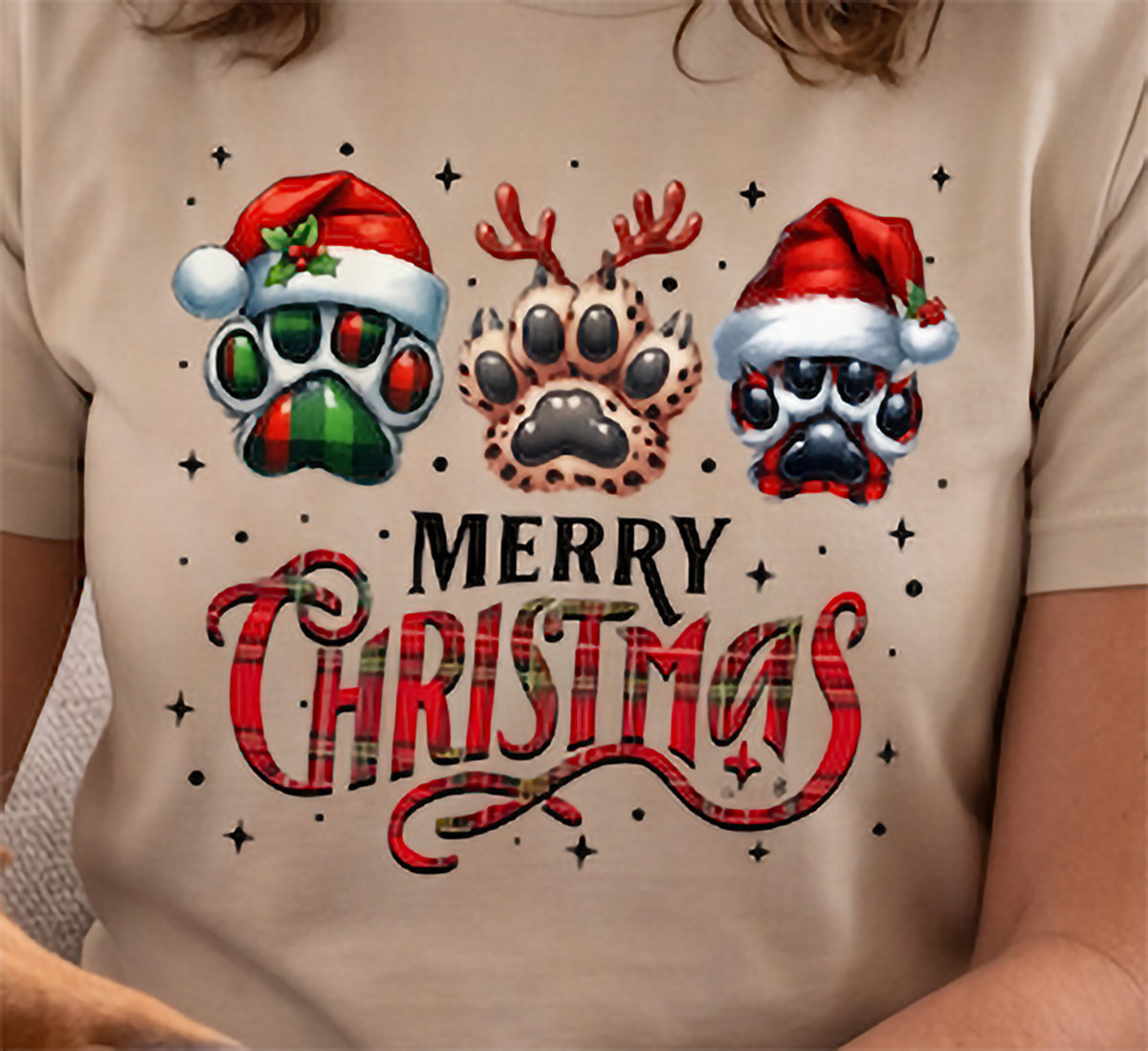 Close-up of sand Merry Christmas dog paw print shirt with Santa hats, antlers and plaid Christmas details.