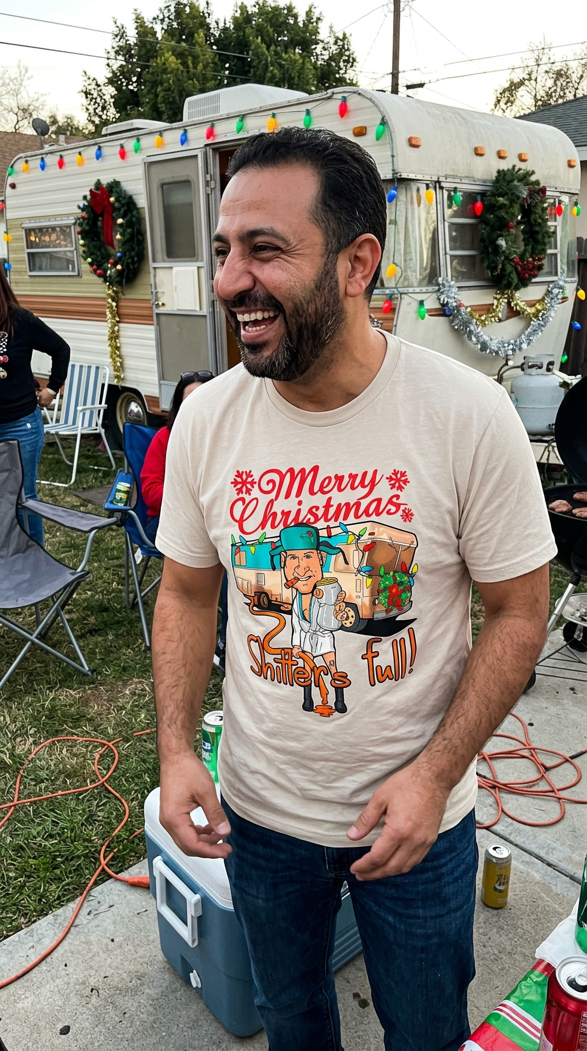 Lifestyle – Heather Gray: Man wearing a heather gray funny Christmas graphic tee featuring a festive camper design at a holiday gathering.