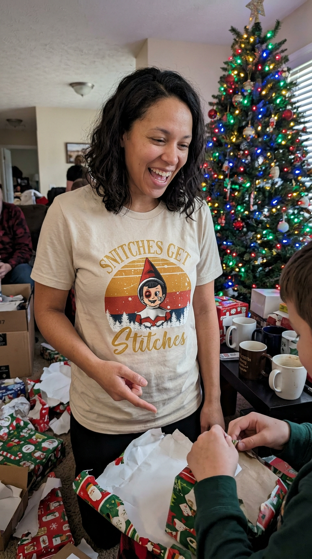 Woman wearing a sand-colored Snitches Get Stitches Christmas shirt while wrapping holiday presents.