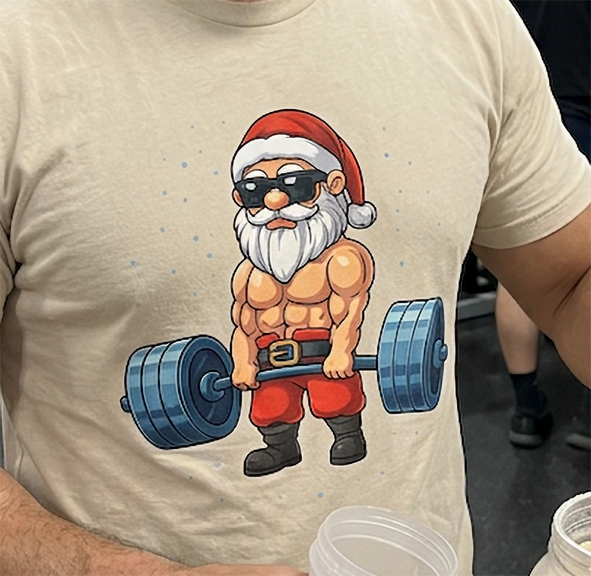 Detailed Swole Santa Christmas weightlifting design on a sand-colored unisex graphic t-shirt.