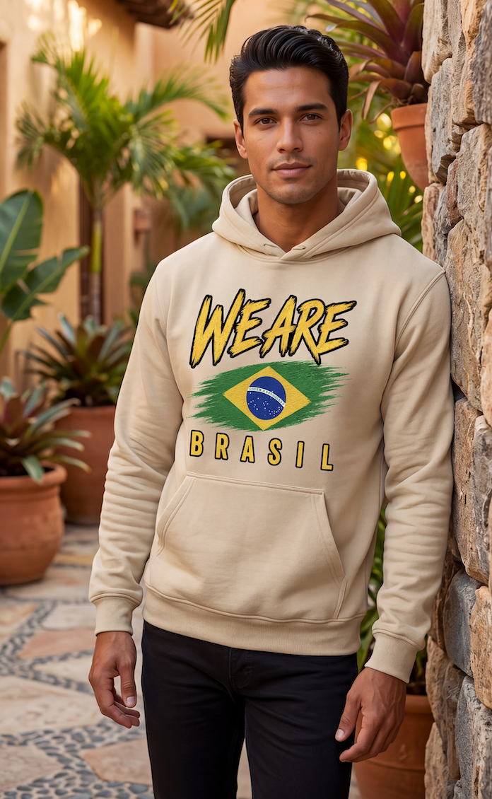 A man wearing a beige hoodie with a 'WE ARE BRASIL' graphic featuring the Brazilian flag, standing outdoors against a stone wall.