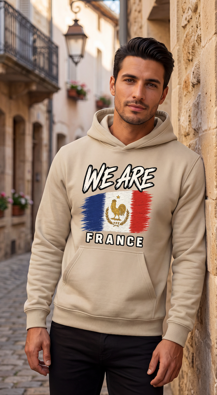A man wearing a beige hoodie with a 'WE ARE FRANCE' graphic featuring the French flag and rooster emblem, standing in a stone alleyway.