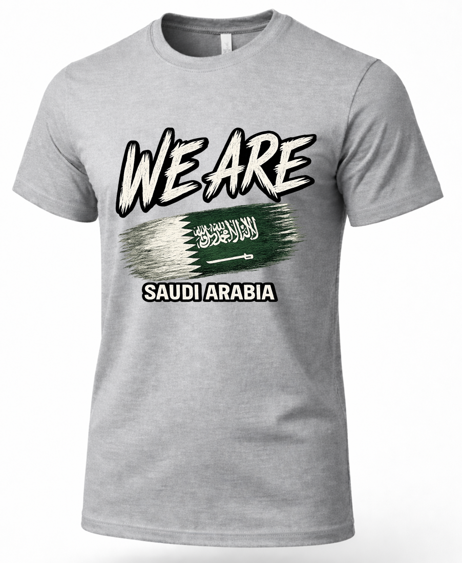A heather gray short-sleeve t-shirt with a graphic print on the front. The design features the text 'WE ARE' in a bold, stylized white font with black outlines, above a green and white brushstroke design resembling the Saudi Arabian flag, with 'SAUDI ARABIA' printed below in white.