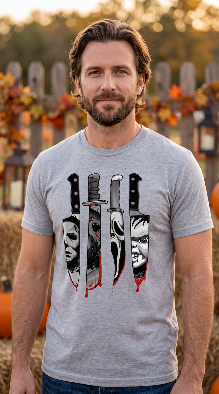 A man wearing a heather gray short-sleeve crewneck t-shirt featuring a graphic print of four horror movie knives dripping with red blood, each filled with a stylized black and white face (Michael Myers, Jason Voorhees, Freddy Krueger, and Pennywise).