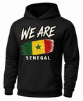 A black pullover hoodie featuring a distressed graphic print of the Senegalese flag with the text 'WE ARE' above and 'SENEGAL' below, shown on a plain white background.