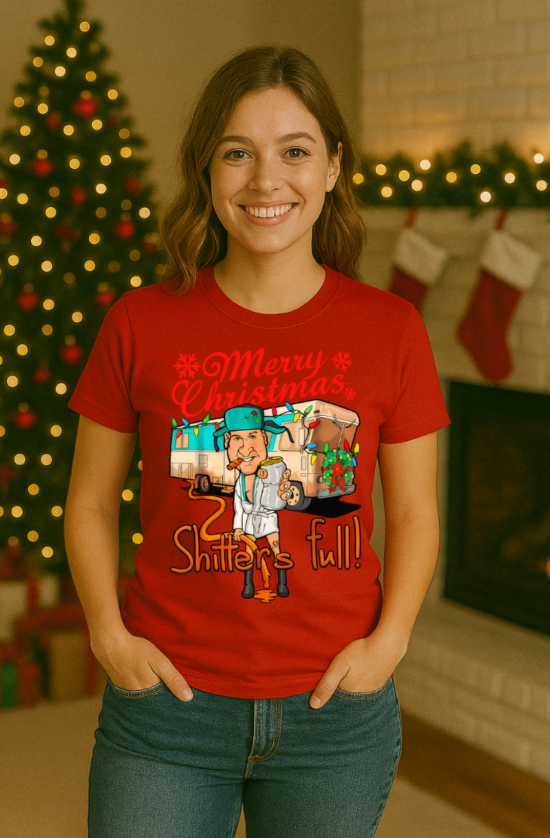 Smiling woman wearing a red “Merry Christmas, Shitter’s Full” graphic t-shirt, standing in front of a decorated Christmas tree and fireplace with stockings and holiday lights.