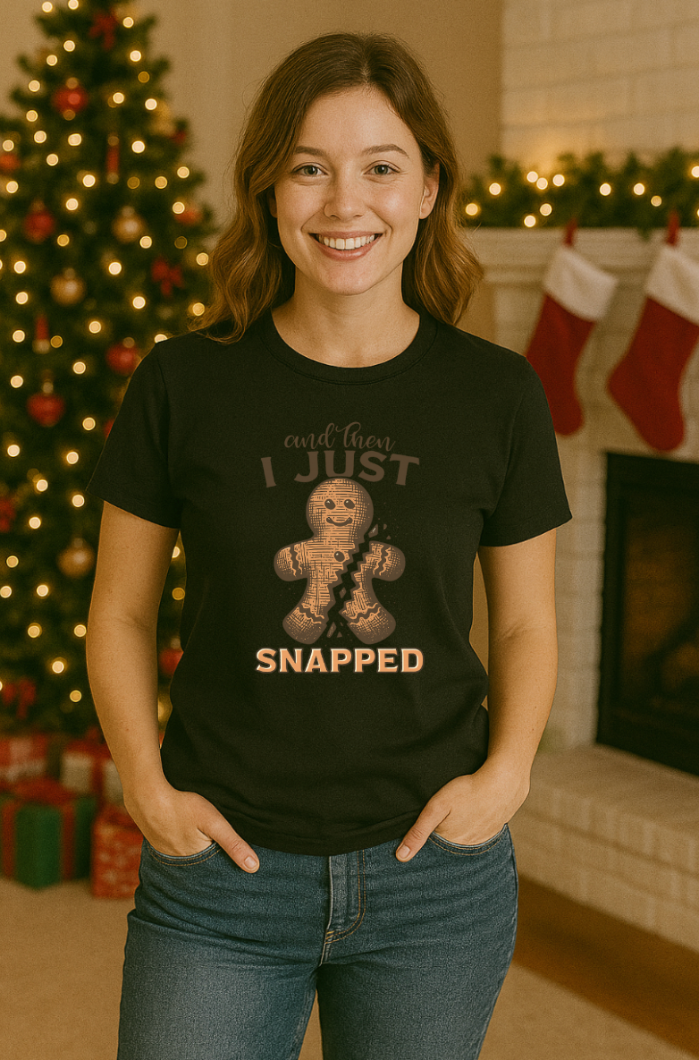 Woman wearing a black “And Then I Just Snapped” gingerbread Christmas shirt, standing in a festive holiday room with a decorated Christmas tree and stockings.