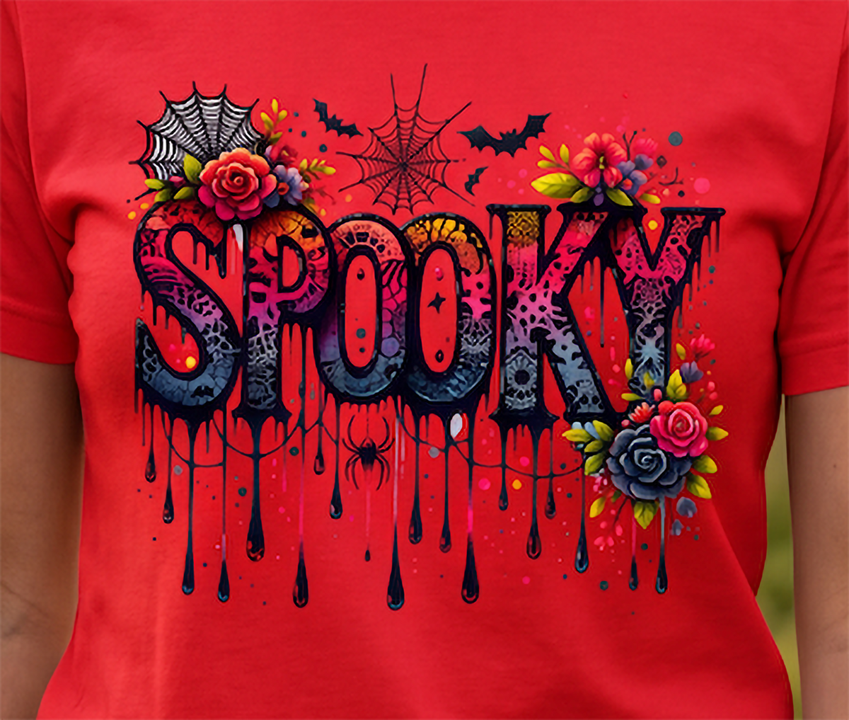 A close-up of a red short-sleeve T-shirt worn by a person, featuring a large Halloween-style 'Spooky' graphic with dripping black lettering, roses, flowers, spiders, bats, and spiderwebs.
