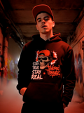 Man wearing black “Stay True Stay Real” skull graphic hoodie in a graffiti alley streetwear setting