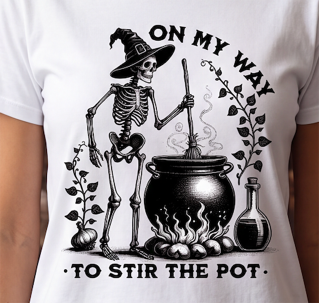 A white short-sleeve crewneck t-shirt featuring a black graphic print of a skeleton wizard stirring a cauldron with the text 'ON MY WAY TO STIR THE POT'.
