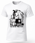 A white short-sleeve crewneck t-shirt featuring a black graphic of a skeleton wizard stirring a cauldron with the text 'ON MY WAY TO STIR THE POT'.
