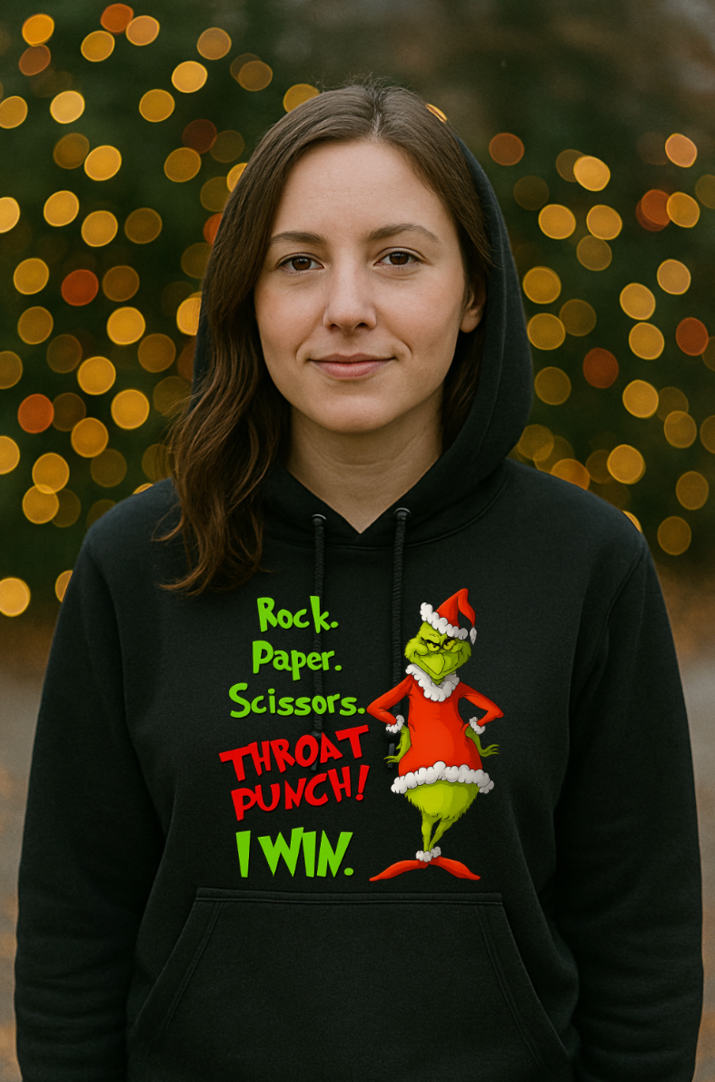 Woman wearing a black Christmas hoodie with a funny Rock Paper Scissors Throat Punch design, standing in front of a blurred holiday lights background.
