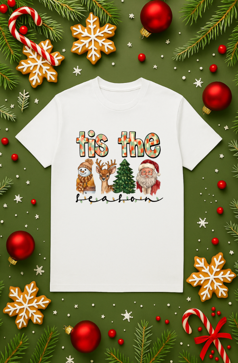 White unisex Christmas graphic tee with “’tis the season” design featuring a snowman, reindeer, Christmas tree, and Santa, displayed on a green holiday background with ornaments, candy canes, and snowflakes.